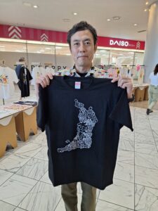 MOJIMAP Tシャツを手に持つ浦泉裕一
